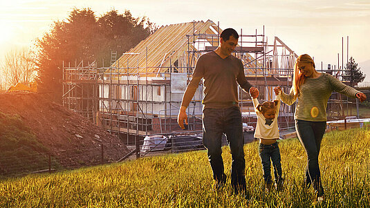 Familie entdeckt Grundstück im Landkreis Verden mit Contura Bau Familie steht auf einer Wiese vor einer Baustelle und freut sich auf den Hausbau im Landkreis Verden mit Contura Bau
