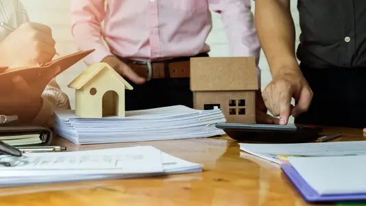 Hausbauplanung in Verden Personen planen ein Hausbauprojekt mit Hausmodellen, Bauunterlagen und Taschenrechner in Verden.