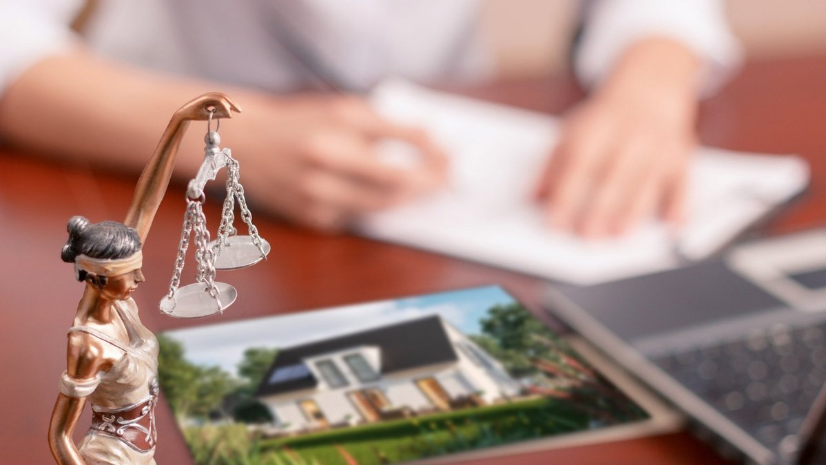 Justitia-Figur mit Waage neben Hausentwurf und Unterlagen zum Baurecht beim Hausbau