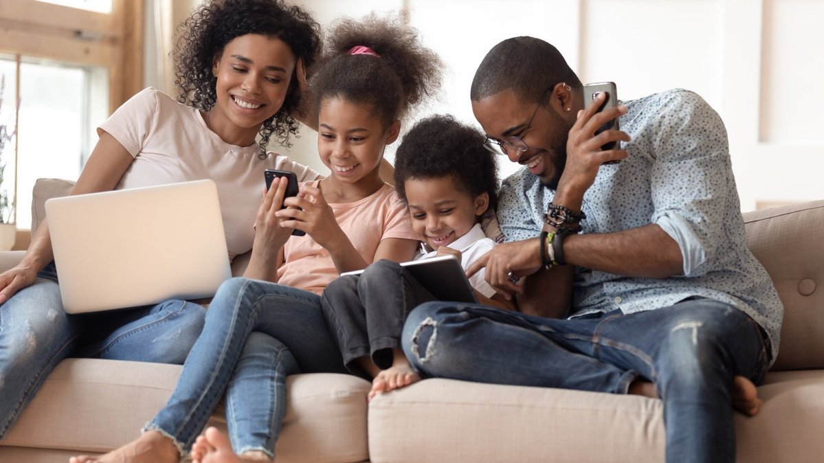 Familie sitzt gemeinsam auf dem Sofa und nutzt Laptop, Smartphone und Tablet als Symbol für digitales Wohnen und Familienalltag in Bruchhausen-Vilsen.