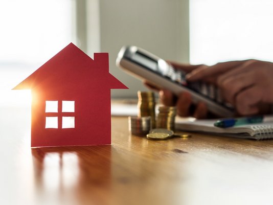 Hausbaufinanzierung und Kostenplanung in Rodewald Rotes Hausmodell mit Münzen, Taschenrechner und Smartphone als Symbol für Hausbaukosten und Finanzierung in Rodewald mit Contura Bau GmbH
