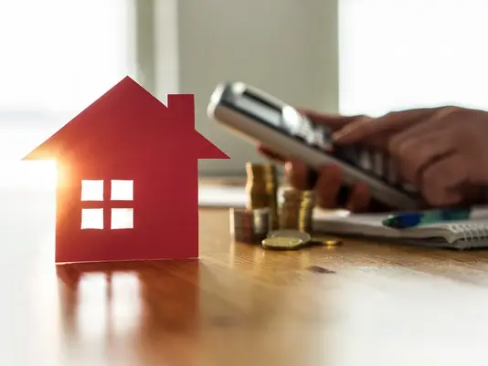 Rotes Hausmodell mit Münzen, Taschenrechner und Smartphone als Symbol für Hausbaukosten und Finanzierung in Rodewald mit Contura Bau GmbH