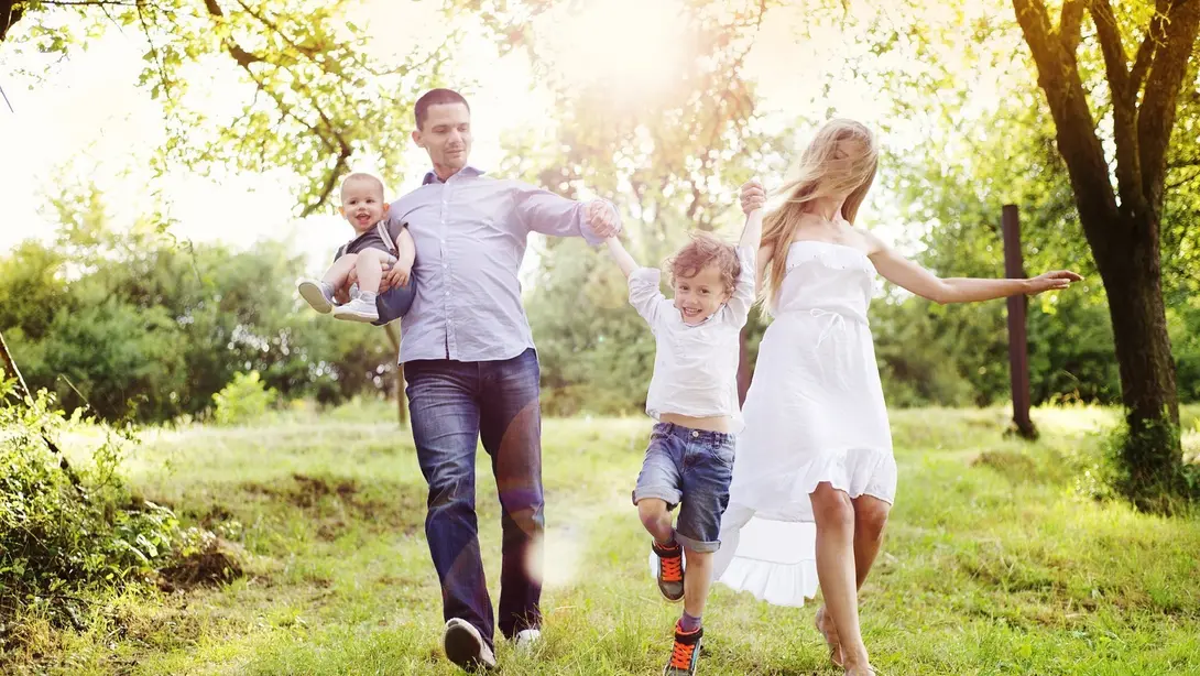 Familie mit zwei Kindern läuft bei Sonnenschein durch eine grüne Wiese in naturnaher Umgebung
