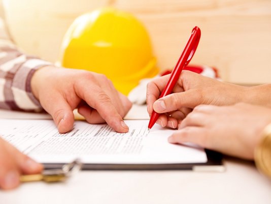 Beratung und Planung für den Hausbau Beratungsgespräch mit Bauunterlagen, Stift und Schutzhelm als Symbol für Hausbauplanung und Vertragsvorbereitung mit Contura Bau GmbH