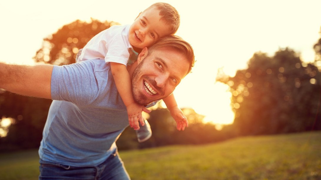 Vater trägt Kind lachend auf den Schultern im Sonnenuntergang