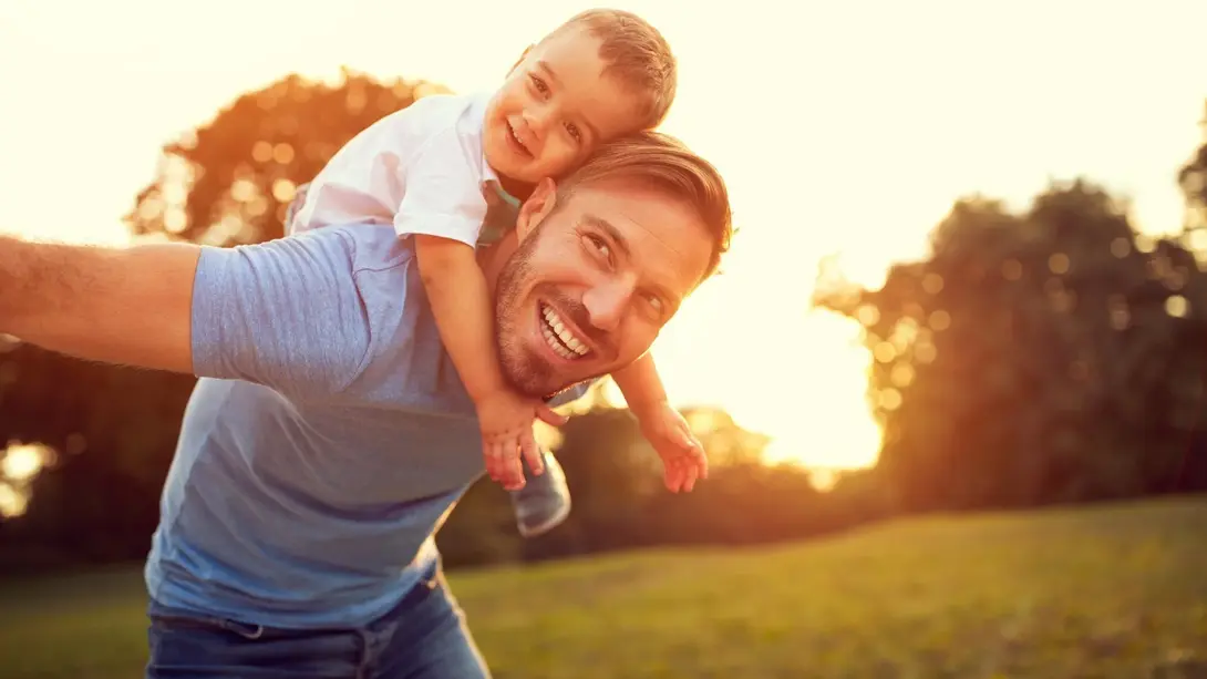 Vater trägt Kind lachend auf den Schultern im Sonnenuntergang