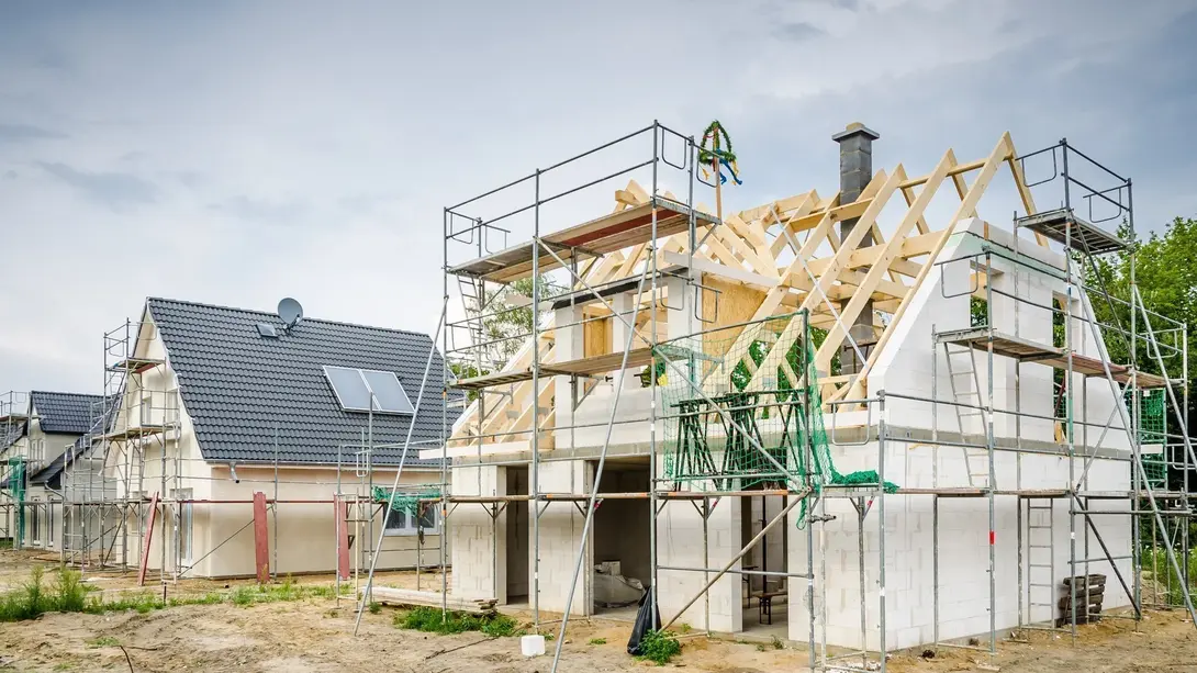 Rohbau eines Einfamilienhauses mit Dachstuhl, Gerüst und Richtkranz als Symbol für den Hausbau mit Contura Bau GmbH
