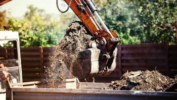 Erdarbeiten zur Vorbereitung eines Baugrundstücks Bagger lädt ausgehobene Erde auf einen Anhänger