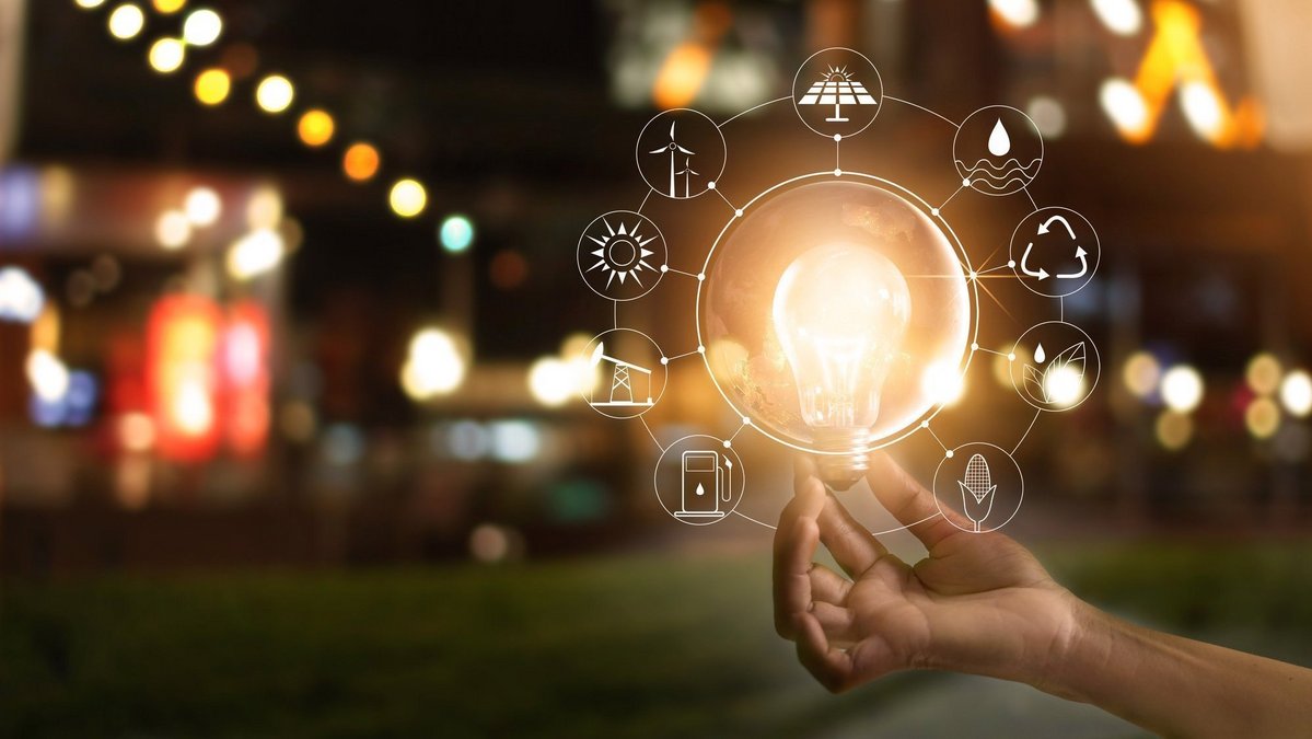 Hand hält eine leuchtende Glühbirne, umgeben von Symbolen für erneuerbare Energien und Nachhaltigkeit