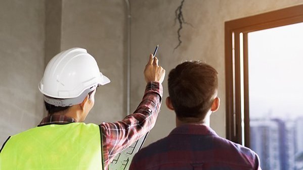 Bauleiter mit Schutzhelm prüft gemeinsam mit Bauherrn eine Wandöffnung im Rohbau