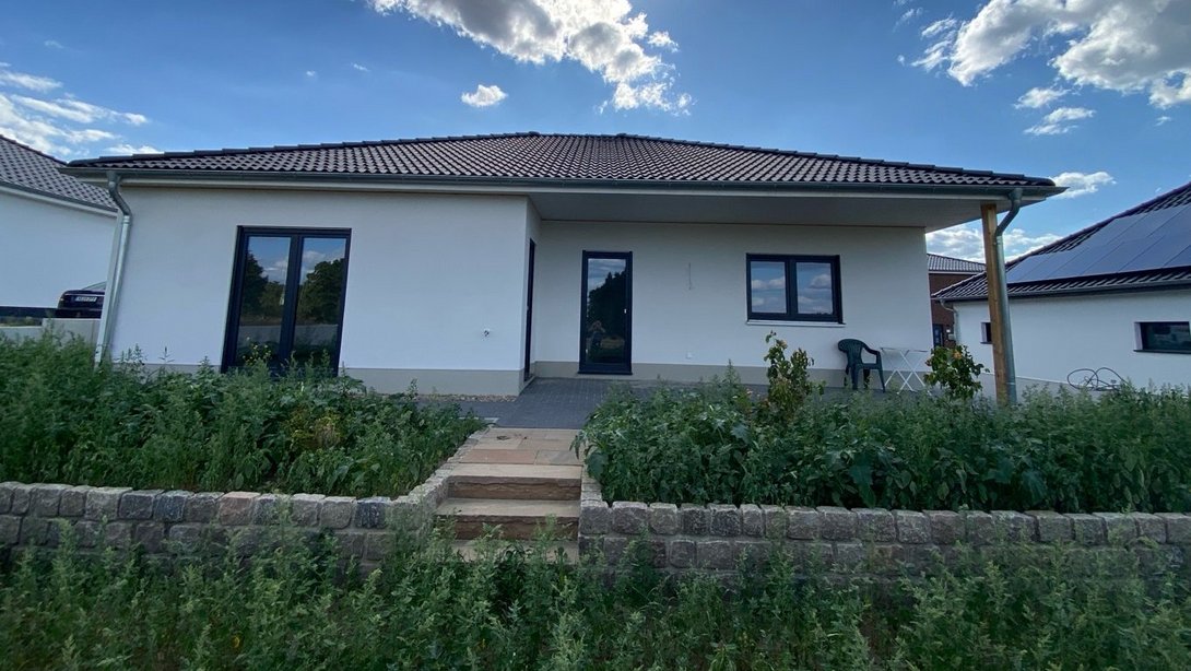 Moderner Bungalow mit heller Fassade, Walmdach, Terrasse und naturnahem Vorgarten als Beispiel für den Hausbau mit Contura Bau GmbH