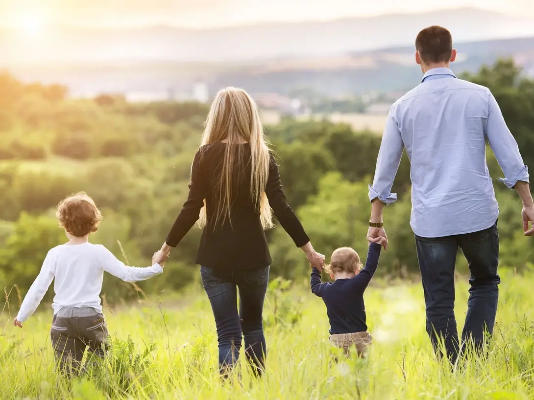 Familienfreundlich wohnen im eigenen Zuhause Familie mit zwei Kindern geht gemeinsam über eine Wiese als Symbol für familienfreundliches Wohnen und den Hausbau mit Contura Bau GmbH
