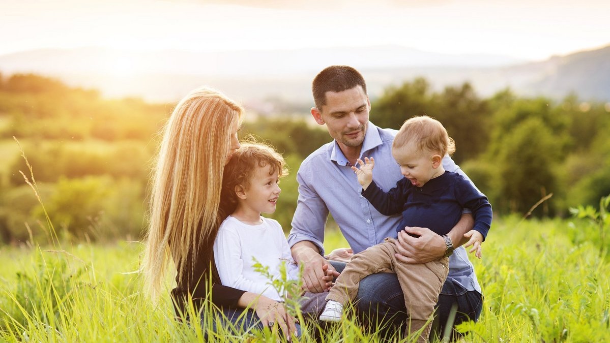 Familienleben im passenden Wohnumfeld Familie mit zwei Kindern sitzt gemeinsam auf einer grünen Wiese in sonniger Landschaft