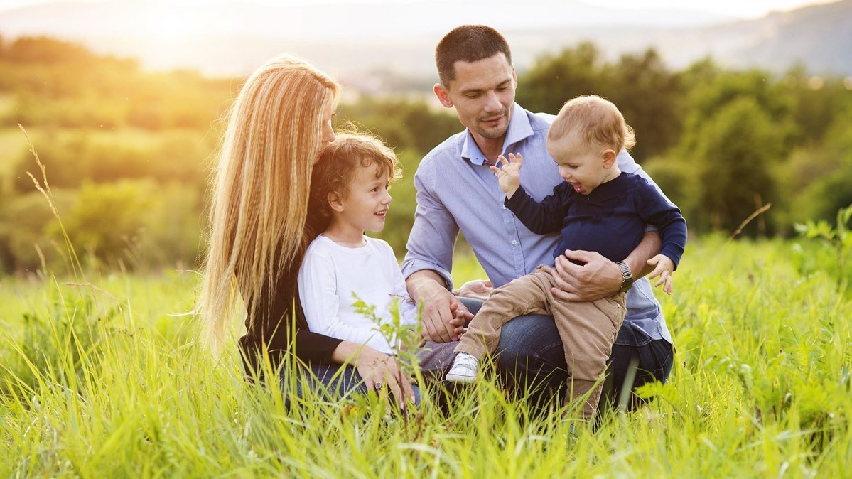 Junge Familie mit zwei Kindern sitzt bei Sonnenuntergang auf einer grünen Wiese