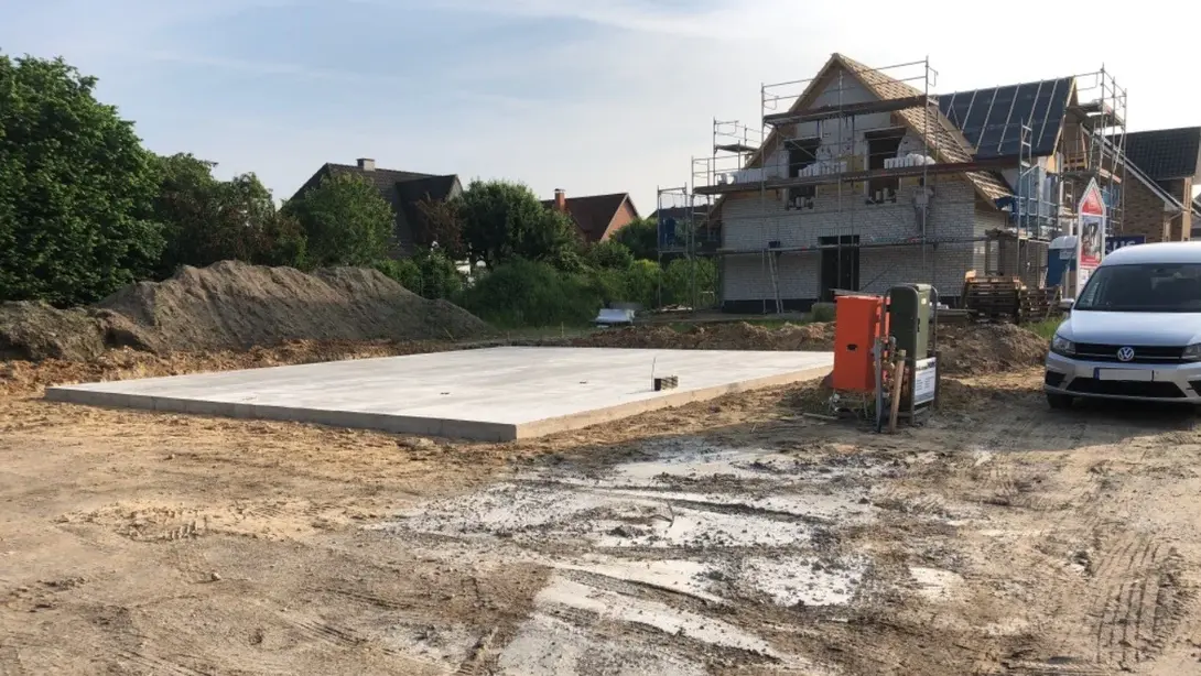 Bodenplatte als Grundlage für den Hausbau Bodenplatte auf einer Baustelle mit Rohbau im Hintergrund