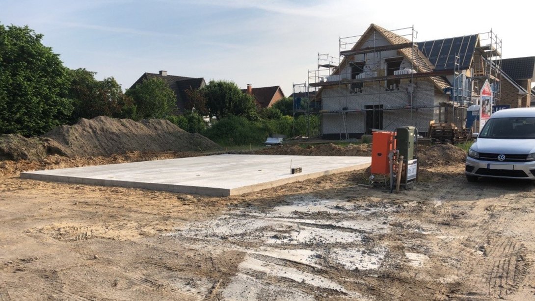 Bodenplatte auf einer Baustelle mit Rohbau im Hintergrund