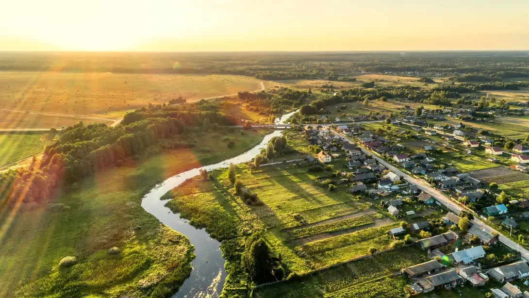 Luftaufnahme einer ländlichen Wohnlage mit Fluss, Feldern und Siedlung bei Sonnenuntergang
