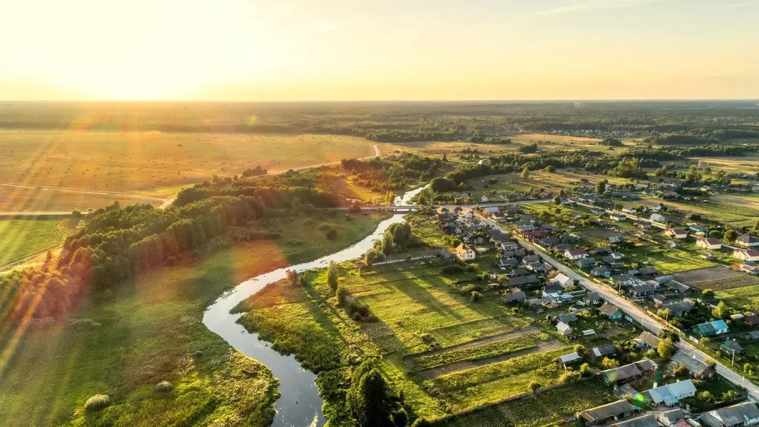 Naturnah wohnen in ländlicher Lage mit Flussnähe Luftaufnahme einer ländlichen Wohnlage mit Fluss, Feldern und Siedlung bei Sonnenuntergang