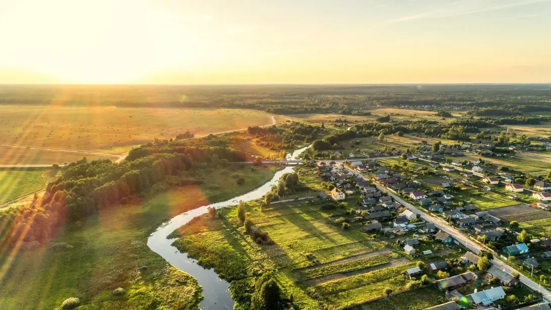 Luftaufnahme einer ländlichen Siedlung mit Fluss, Feldern und Wiesen bei tief stehender Sonne