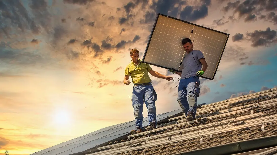 Montage einer Photovoltaikanlage auf dem Dach Zwei Monteure installieren ein Solarmodul auf einem Hausdach