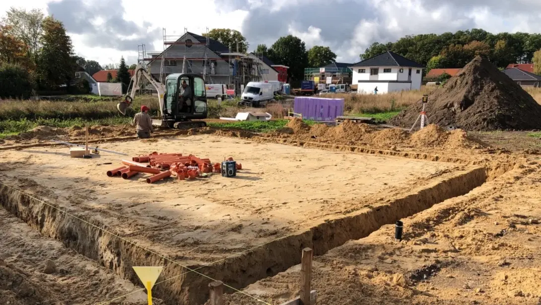Baugrundstück mit ausgehobenen Fundamentgräben, Bagger und vorbereiteten Leitungen während der Bauvorbereitung