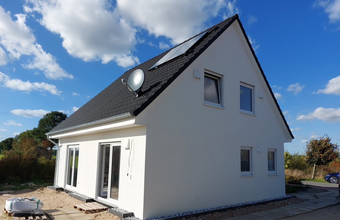 Einfamilienhaus mit weißer Fassade, dunklem Satteldach und großen Terrassentüren im Baugebiet Heemsen.