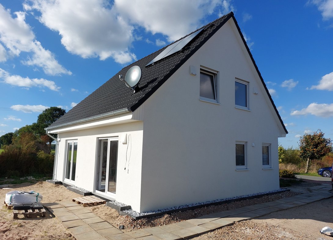 Modernes Einfamilienhaus mit heller Fassade, Satteldach, Photovoltaikanlage und unfertigem Außenbereich als Beispiel für den Hausbau mit Contura Bau GmbH