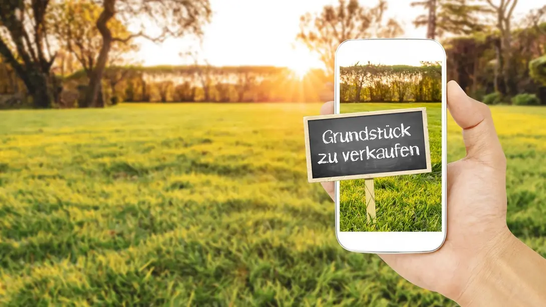 Smartphone zeigt Grundstück zu verkaufen vor grüner Fläche in Martfeld