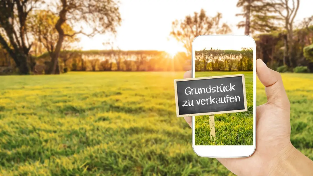 Grundstück zu verkaufen auf grüner Wiese mit Smartphone als Symbol für Bauplatzsuche