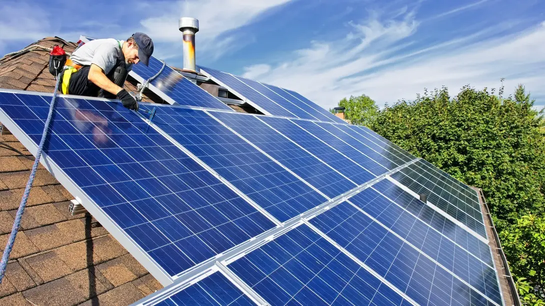 Handwerker montiert Photovoltaikanlage auf einem Hausdach als Symbol für energieeffizientes Bauen