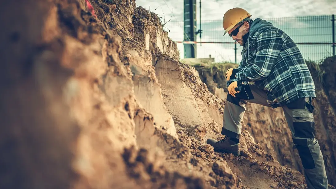 Baugrund und Bodenschichten auf dem Grundstück prüfen Bauarbeiter mit Schutzhelm bei der Begutachtung einer ausgehobenen Baugrube und freigelegter Bodenschichten