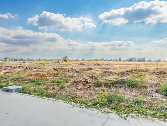 Freies Baugrundstück in offener Lage Unbebautes Grundstück an einer befestigten Straße unter blauem Himmel