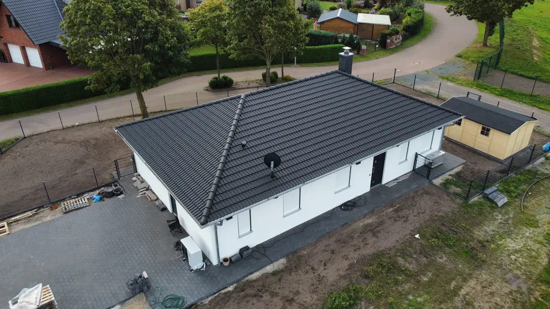 Luftaufnahme eines modernen Bungalows mit heller Fassade, dunklem Walmdach und großzügigem Grundstück als Beispiel für den Hausbau in Leese mit Contura Bau GmbH
