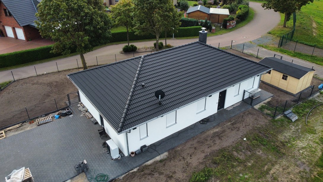 Moderner Bungalow auf großzügigem Grundstück in Leese Luftaufnahme eines modernen Bungalows mit heller Fassade, dunklem Walmdach und großzügigem Grundstück als Beispiel für den Hausbau in Leese mit Contura Bau GmbH