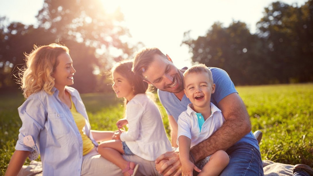 Familienfreundlich wohnen in Leese Familie mit zwei Kindern sitzt gemeinsam auf einer sonnigen Wiese als Symbol für familienfreundliches Wohnen in Leese mit Contura Bau GmbH