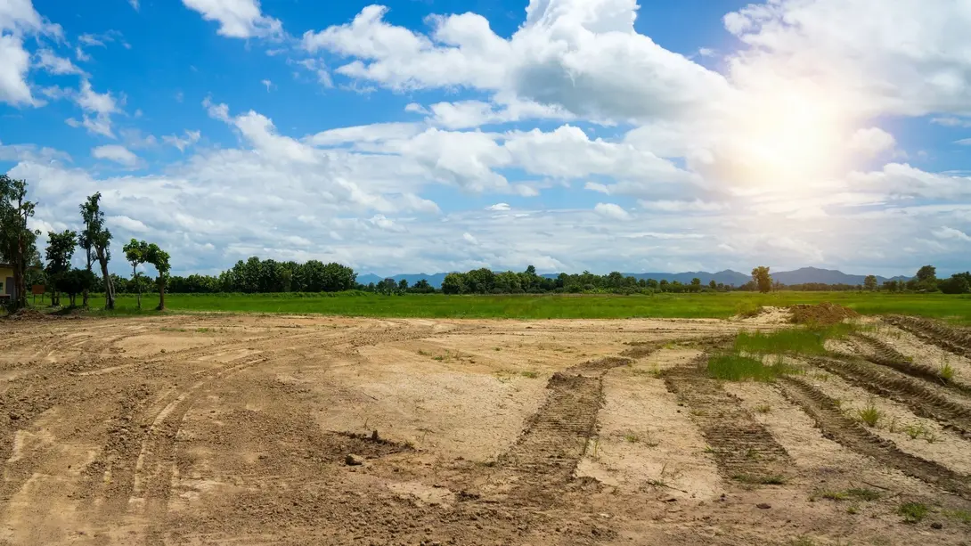 Freie Baufläche für zukünftige Bebauung Freie Baufläche mit Erdarbeiten, Fahrspuren und angrenzenden Grünflächen unter blauem Himmel