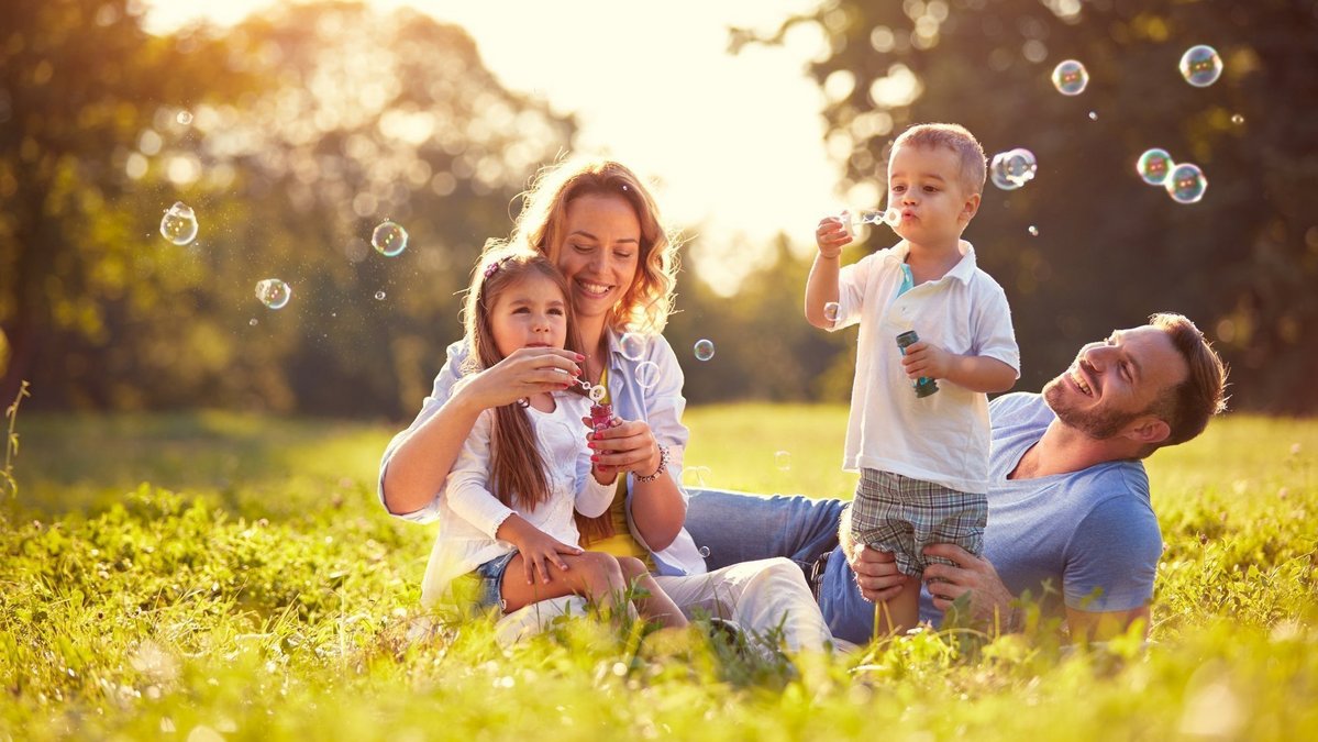 Familienfreundlich wohnen in Pennigsehl Familie sitzt lachend auf einer Wiese und spielt mit Seifenblasen als Symbol für familienfreundliches Wohnen in Pennigsehl.