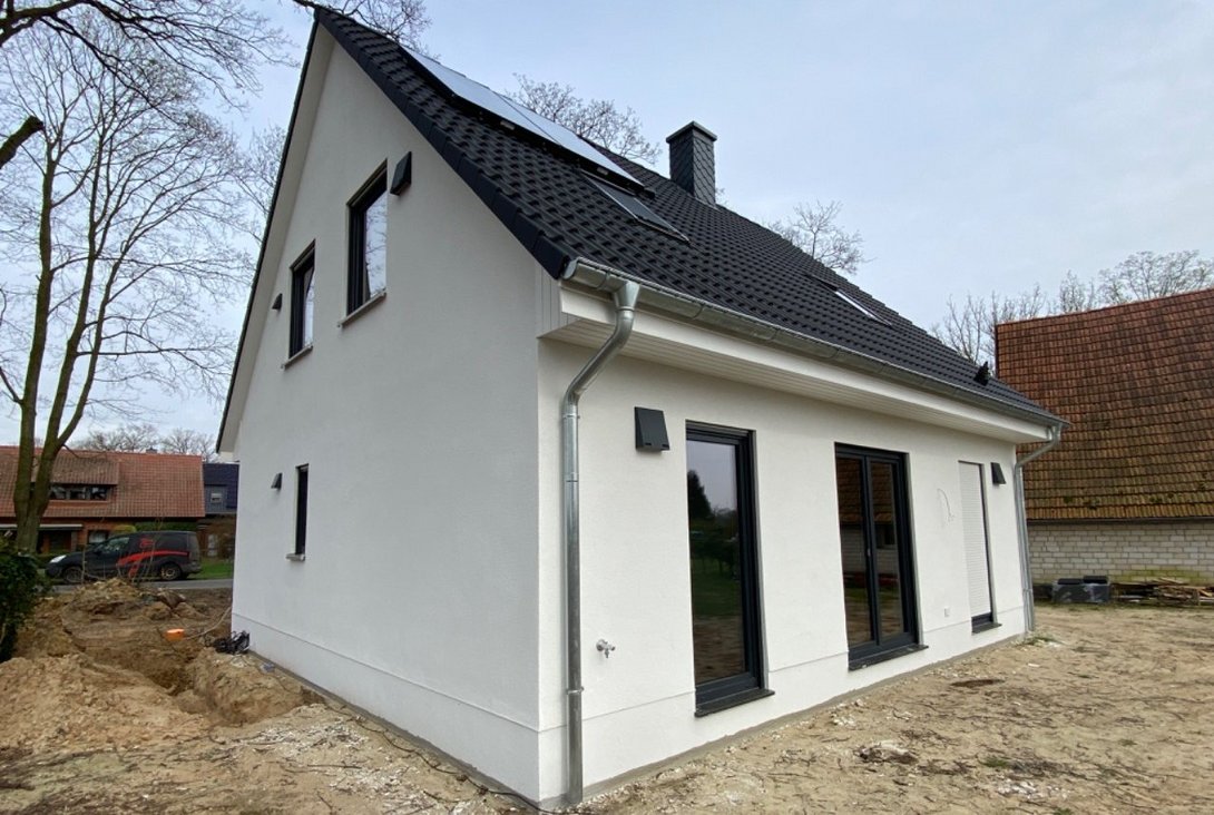 Neubau mit Photovoltaikanlage in Rodewald Modernes Einfamilienhaus mit heller Fassade, Satteldach, Photovoltaikanlage und Baustellenbereich als Beispiel für den Hausbau in Rodewald mit Contura Bau GmbH