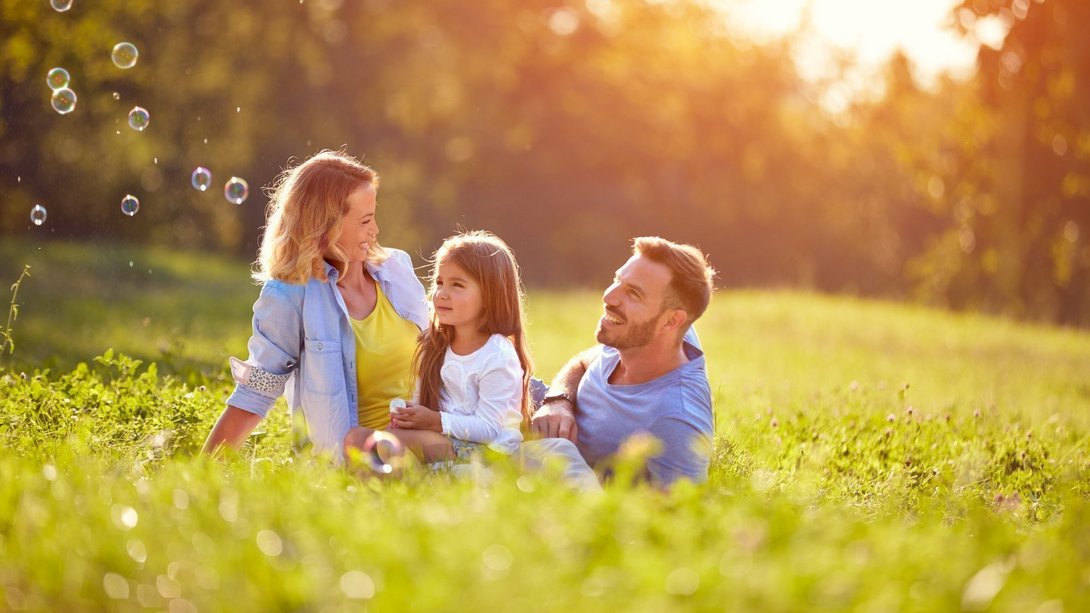 Familienglück im eigenen Zuhause Familie sitzt gemeinsam auf einer sonnigen Wiese als Symbol für naturnahes Wohnen, Lebensqualität und den Hausbau mit Contura Bau GmbH
