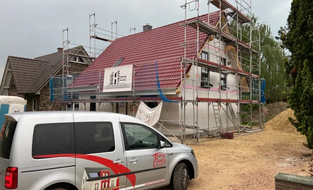 Hausbau mit Contura Bau GmbH in Verden Einfamilienhaus im Bauprozess mit Gerüst, rotem Satteldach und Town & Country Haus Fahrzeug in Verden.