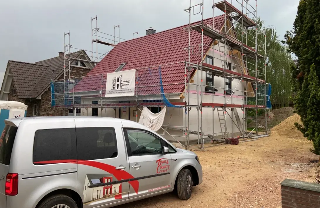 Hausbau in Diepenau mit Contura Bau GmbH Einfamilienhaus im Bauprozess mit Gerüst, rotem Satteldach und Town & Country Haus Fahrzeug auf einer Baustelle in Diepenau.