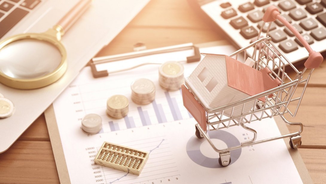 Hauskauf und Baufinanzierung in Stolzenau planen Hausmodell in einem Einkaufswagen auf Finanzunterlagen mit Münzen, Taschenrechner und Lupe als Symbol für Immobilienkauf und Baufinanzierung in Stolzenau.