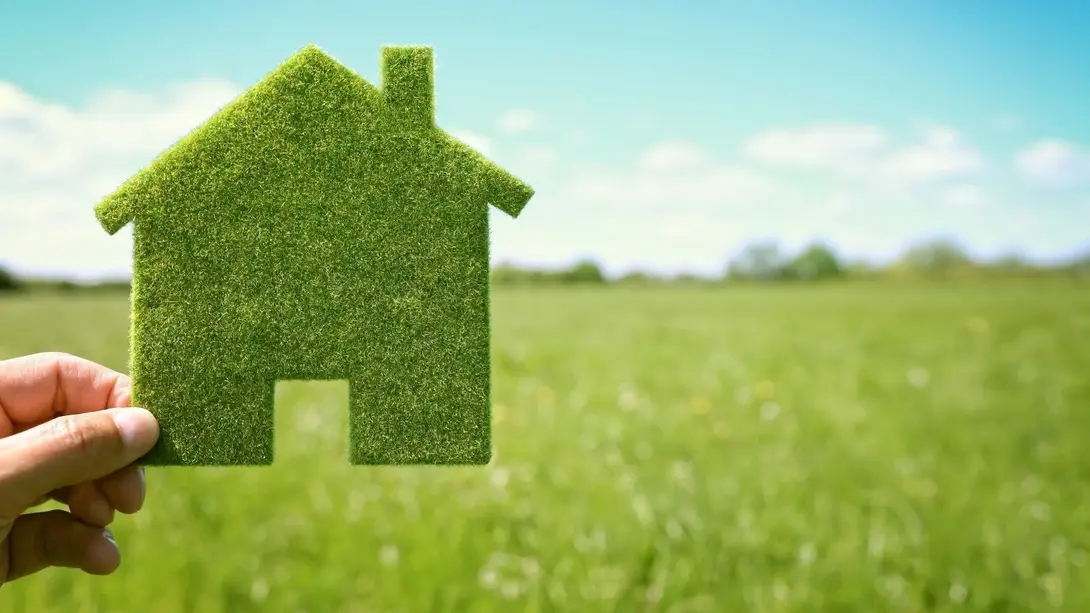 Nachhaltig bauen und wohnen im Grünen Grünes Haus-Symbol vor Wiese als Zeichen für nachhaltiges Wohnen