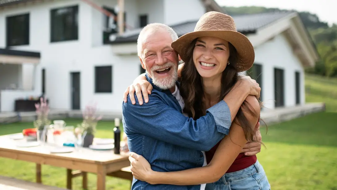 Vater und Tochter umarmen sich lachend im Garten vor einem modernen Einfamilienhaus
